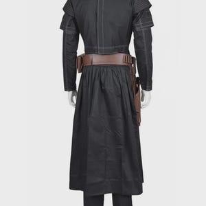 Pode incluir: Um casaco preto de manga comprida com costuras brancas, combinado com uma saia e cal&ccedil;as pretas a condizer. Um cinto utilit&aacute;rio castanho largo com um coldre &eacute; usado &agrave; volta da cintura. O casaco apresenta ombros estruturados e um design.