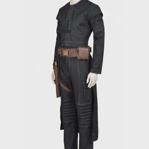 Pode incluir: Uma blusa preta de manga comprida e cal&ccedil;as a condizer com costuras brancas em contraste, pain&eacute;is canelados nos ombros e joelhos, e um cinto utilit&aacute;rio castanho com fivela retangular, uma pequena bolsa e um coldre na lateral das cal&ccedil;as.