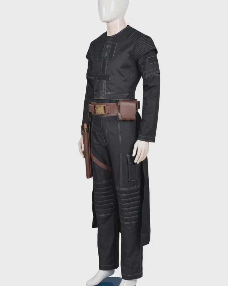 Pode incluir: Uma blusa preta de manga comprida e cal&ccedil;as a condizer com costuras brancas em contraste, pain&eacute;is canelados nos ombros e joelhos, e um cinto utilit&aacute;rio castanho com fivela retangular, uma pequena bolsa e um coldre na lateral das cal&ccedil;as.