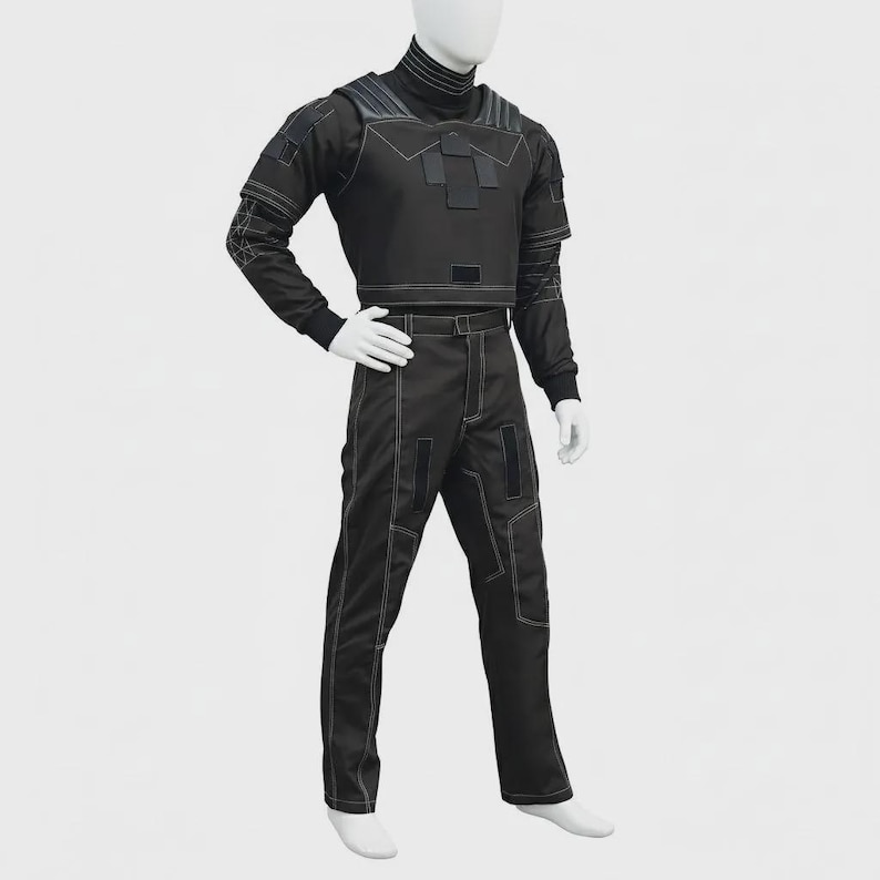 May include: A black tactical-style two-piece outfit consisting of a long-sleeved top and matching trousers. The garment features a high collar, structured chest panel with rectangular accents, and visible white contrast stitching throughout the design.