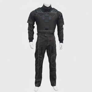 May include: A black tactical-style uniform set consisting of a long-sleeved top with a high collar, shoulder padding, and rectangular patches, paired with matching trousers featuring reinforced stitching, belt loops, and vertical rectangular patches.
