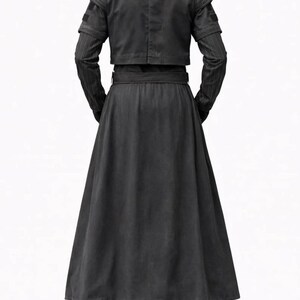 May include: A black long-sleeved jacket and a matching floor-length skirt. The jacket features a cropped cut with ribbed shoulder detailing and vertical pinstripes on the sleeves. The skirt is high-waisted with a wide belt and a flared hem.