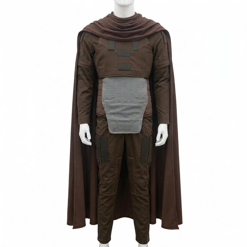 May include: A brown costume set featuring a long cape, a long-sleeved top with dark rectangular chest accents, a light grey abdominal plate, and matching brown trousers with dark rectangular thigh panels, displayed on a white mannequin torso.