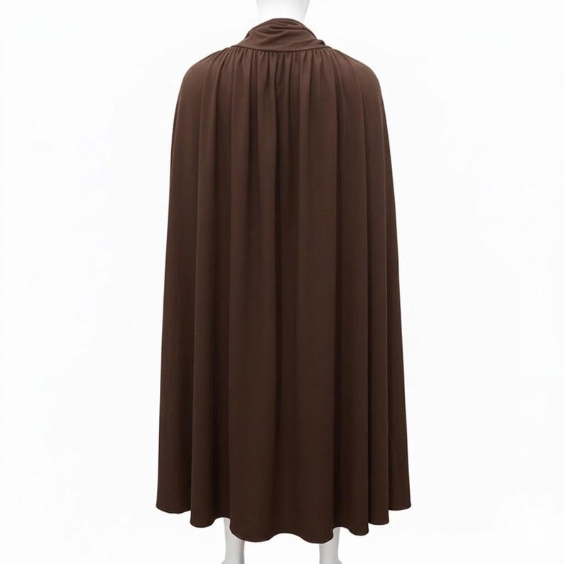 May include: A floor-length brown cape featuring a gathered neckline with a draped collar. The garment is constructed from a solid-coloured fabric that hangs in vertical folds, extending from the shoulders down to the hemline in a full silhouette.