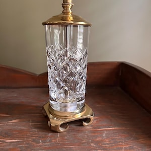 May include: A vintage lamp with a clear, diamond-cut glass shade and a brass base and top. The lamp has a classic design, suitable for a bedside table or desk. The brass base has a decorative, curved design.