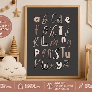 May include: A framed wall art print featuring a dark gray background with the alphabet displayed in a mix of light pink, cream, and brown handwritten-style letters. Some letters incorporate heart shapes, and the print is housed in a light wood frame.