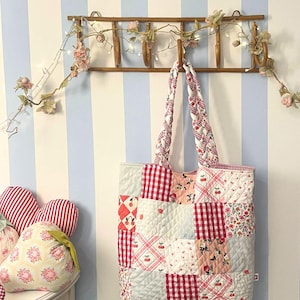 Può includere: Una borsa tote trapuntata con un design patchwork composto da quadretti vichy rossi e bianchi, stampe a ciliegie e motivi floreali. La borsa presenta due manici in tessuto intrecciato ed è realizzata con pannelli quadrati cuciti a griglia.