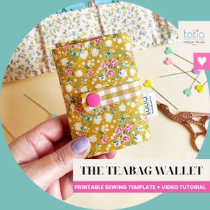 Può includere: Un piccolo portafoglio in tessuto con sfondo giallo senape e un motivo floreale di rose rosa e fiori bianchi. Presenta un cinturino a quadretti beige e bianco fissato con un bottone a pressione rosa acceso. Il testo recita THE TEABAG WALLET.