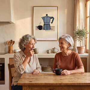 May include: Two women seated at a wooden table, enjoying coffee. A framed print on the wall depicts a coffee maker and cup. The print has the text "PRENDIAMO UN CAFFÈ". The room has a warm, inviting atmosphere with natural light.