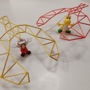 May include: A playful scene featuring two geometric structures, one yellow and one red, with Mario and Yoshi figurines. The yellow structure is near Mario, who is wearing a red outfit and white hat. Yoshi is near the red structure.