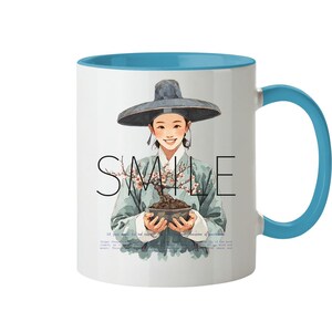 Può includere: Tazza in ceramica bianca con interno e manico blu. La tazza presenta un'illustrazione di una persona con un cappello che tiene un bonsai. La parola "SMILE" è scritta sulla tazza.