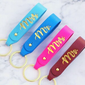 Pode incluir: Quatro chaveiros de couro com letras douradas. Os chaveiros são azuis, rosa e bordô. As letras dizem "Sra." e "Sr."