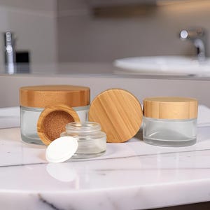 Peut inclure: Plusieurs pots en verre transparent avec des couvercles en bambou sont présentés. Un pot a un intérieur en bois et un autre un couvercle blanc. Les pots sont vides, adaptés au stockage de cosmétiques ou de petits articles.