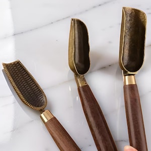 Puede incluir: Tres cucharas de té con cuencos de color latón y mangos de madera oscura. Las cucharas tienen una estética vintage, con un patrón texturizado en una cuchara. Los mangos están conectados a los cuencos con una banda dorada.