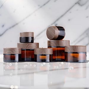 May include: An assortment of amber glass jars with wooden lids. The jars are arranged in a group, varying in size, and are set against a white marble background. The lids have a natural wood grain appearance.