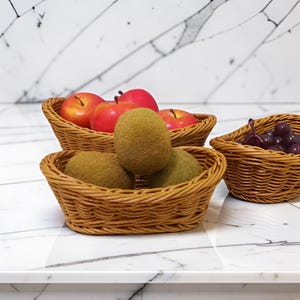 May include: Three woven wicker baskets filled with fruit. The baskets contain red apples, green kiwis, and purple grapes. The baskets are arranged on a white marble surface.
