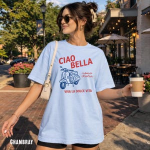 May include: Light blue chambray t-shirt with a graphic of a scooter and the words "CIAO BELLA" in red, "roma italia" and "VIVA LA DOLCE VITA" in blue. The shirt is a casual style.