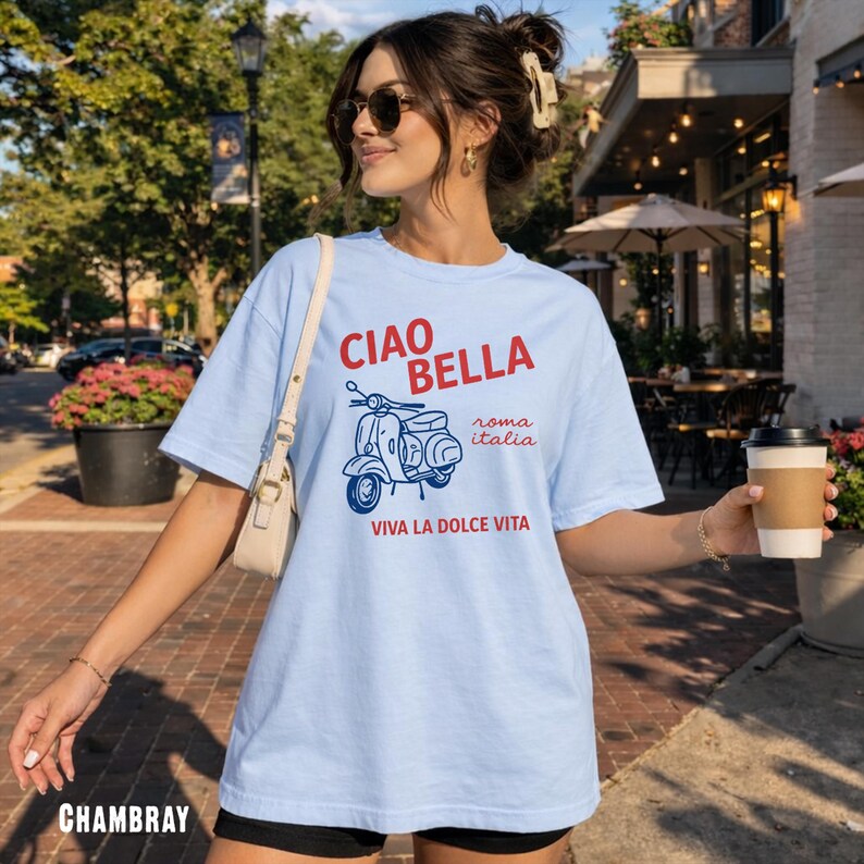 May include: Light blue chambray t-shirt with a graphic of a scooter and the words "CIAO BELLA" in red, "roma italia" and "VIVA LA DOLCE VITA" in blue. The shirt is a casual style.