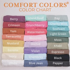 May include: A color chart displaying a variety of Comfort Colors t-shirts. The chart features a range of colors, including Berry, Crimson, and Mustard. The text "COMFORT COLORS COLOR CHART" is at the top.