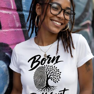 May include: A white short-sleeved t-shirt featuring a black graphic print. The design displays the text "Born Different" with a central image that merges a human fingerprint on the left side with a leafy tree on the right side.