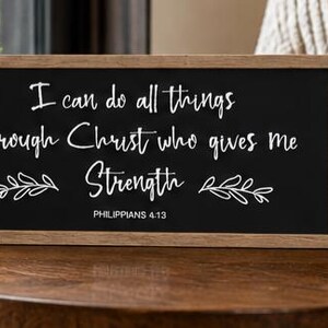 May include: A rectangular wooden-framed sign with a black background and white text that reads I can do all things through Christ who gives me Strength PHILIPPIANS 4:13, accompanied by a white ceramic mug with the text Good Things Ahead.