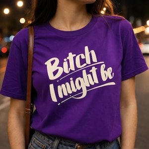 May include: A purple t-shirt with the text "Bitch I might be" in a white, stylized font. The shirt is a crew neck style and appears to be made of a soft material. The image is taken outdoors at night.