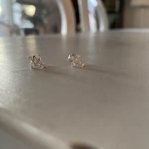 May include: A pair of silver earrings with small, clear stones set in a cross shape.