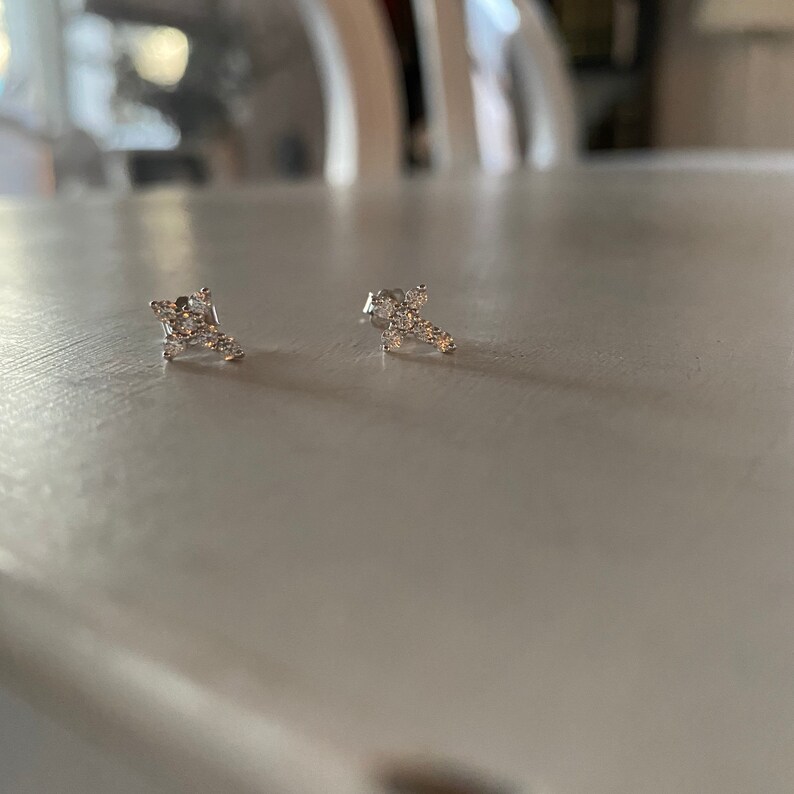 May include: A pair of silver earrings with small, clear stones set in a cross shape.