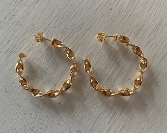 May include: A pair of gold-toned twisted hoop earrings. The earrings are made of a thick, twisted wire and have a simple, modern design.