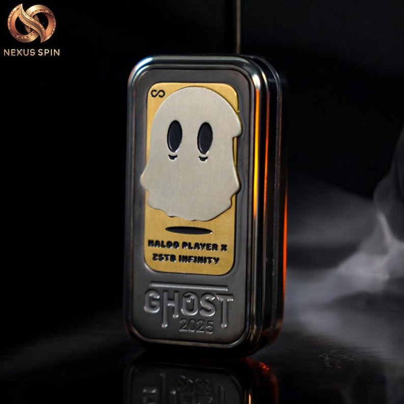 May include: A rectangular, metallic object with a gold and silver finish. The front features a ghost design with the text "HALOO PLAYER X ZSTB INFINITY" and "GHOST 2025". The object has a sleek, modern design.