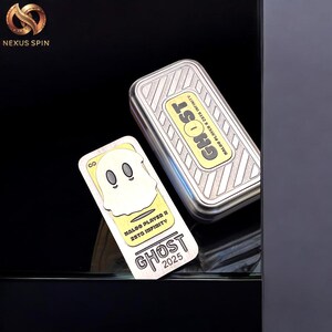May include: A silver rectangular box and a matching card with a ghost design. The box and card have the word "GHOST" in yellow and black. The card also has the text "NALOO PLAYER X 2STD INFINITY" and "2025".