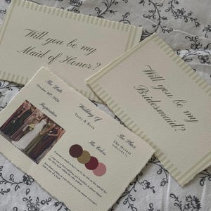 Peut inclure: Cartes d'invitation ivoire avec bords irréguliers. Les cartes présentent les textes « Will you be my Maid of Honor? » et « Will you be my Bridesmaid? ». Une carte comprend des détails de mariage, des échantillons de couleurs et une photo.