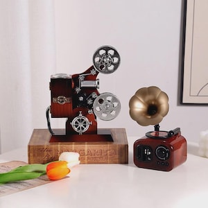 May include: A vintage-style wooden projector and a gramophone-shaped speaker. The projector has silver reels and a dark brown finish. The speaker has a gold horn and a red-brown base. The base of the projector has the text "The Margarita Book".