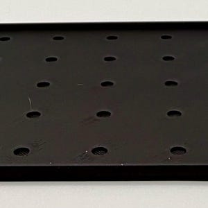 K&ouml;nnte beinhalten: Ein schwarzes rechteckiges Tablett mit einem Gitter aus gleichm&auml;&szlig;ig verteilten L&ouml;chern. Das Tablett hat einen erh&ouml;hten Rand und eine matte Oberfl&auml;che. Die L&ouml;cher sind kreisf&ouml;rmig und scheinen gleichm&auml;&szlig;ig gro&szlig; zu sein. Das Tablett ist wahrscheinlich aus Metall oder einem &auml;hnlichen Material.