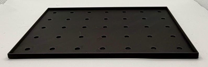 K&ouml;nnte beinhalten: Ein schwarzes rechteckiges Tablett mit einem Gitter aus gleichm&auml;&szlig;ig verteilten L&ouml;chern. Das Tablett hat einen erh&ouml;hten Rand und eine matte Oberfl&auml;che. Die L&ouml;cher sind kreisf&ouml;rmig und scheinen gleichm&auml;&szlig;ig gro&szlig; zu sein. Das Tablett ist wahrscheinlich aus Metall oder einem &auml;hnlichen Material.