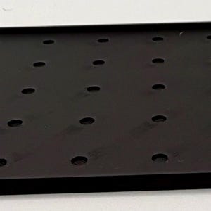 K&ouml;nnte beinhalten: Ein rechteckiger schwarzer Tablett mit erh&ouml;htem Rand und zahlreichen gleichm&auml;&szlig;ig verteilten kreisf&ouml;rmigen L&ouml;chern. Das Tablett besteht aus einem matten Material und liegt auf einer wei&szlig;en Oberfl&auml;che. Die L&ouml;cher sind klein und gleichm&auml;&szlig;ig gro&szlig;.