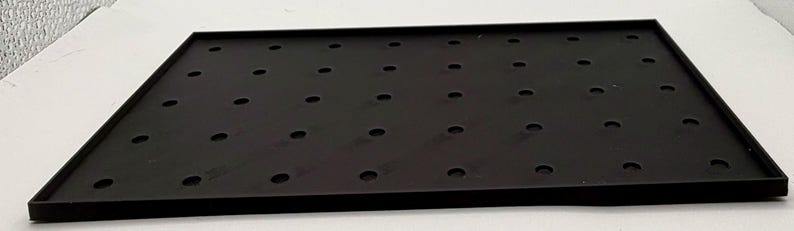 K&ouml;nnte beinhalten: Ein rechteckiger schwarzer Tablett mit erh&ouml;htem Rand und zahlreichen gleichm&auml;&szlig;ig verteilten kreisf&ouml;rmigen L&ouml;chern. Das Tablett besteht aus einem matten Material und liegt auf einer wei&szlig;en Oberfl&auml;che. Die L&ouml;cher sind klein und gleichm&auml;&szlig;ig gro&szlig;.