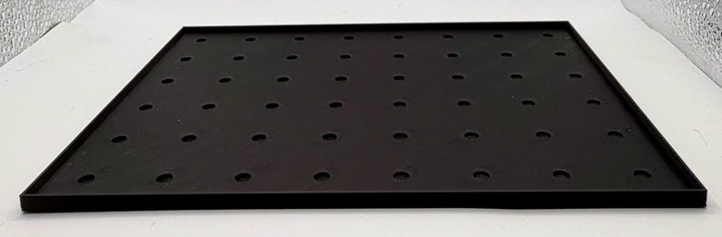 K&ouml;nnte beinhalten: Ein schwarzes quadratisches Tablett mit erh&ouml;htem Rand und zahlreichen, gleichm&auml;&szlig;ig verteilten kreisf&ouml;rmigen L&ouml;chern. Das Tablett besteht aus einem matten Material und liegt auf einer wei&szlig;en Oberfl&auml;che. Die Abmessungen des Tabletts betragen ca. 30 cm x 30 cm.