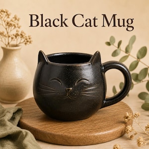 May include: A black ceramic mug shaped like a cat head with pointed ears, a curved handle, and an embossed smiling face with whiskers. The text Black Cat Mug is printed above the mug in a dark brown serif font on a light beige background.