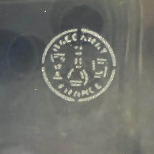 May include: A circular, white emblem with the text "FRANCE" and other indiscernible text. The emblem features a central design with geometric shapes, including a triangle and a rectangle. The background is a dark, possibly black, surface.
