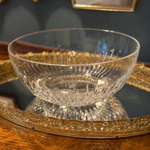 May include: A clear glass bowl with a textured, ribbed design. The bowl sits on a gold-colored, ornate tray. The bowl is reflecting the light, creating a sparkling effect. The bowl is likely used for serving or display.
