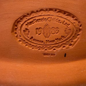 Puede incluir: Una base de cer&aacute;mica color terracota con un sello ovalado en relieve que dice MacKenzie-Childs, Ltd. 1983 Aurora, New York, con un logotipo central y motivos de trigo. Debajo del &oacute;valo, el texto 1997 BH est&aacute; claramente impreso en la arcilla.