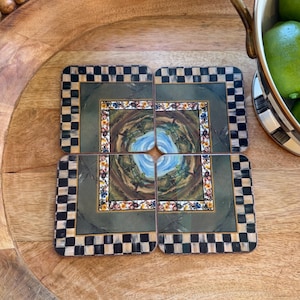 Puede incluir: Juego de cuatro posavasos cuadrados con un diseño decorativo. Cada posavasos presenta una imagen central de un paisaje con un cielo azul y un borde floral. Los bordes tienen un patrón de cuadros blancos y negros.