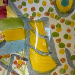 Puede incluir: Un cuenco de cer&aacute;mica con un dise&ntilde;o abstracto pintado a mano sobre una base blanca. La superficie est&aacute; decorada con puntos circulares amarillos, verdes y marrones, junto con formas geom&eacute;tricas azules y amarillas y acentos lineales gris oscuro.