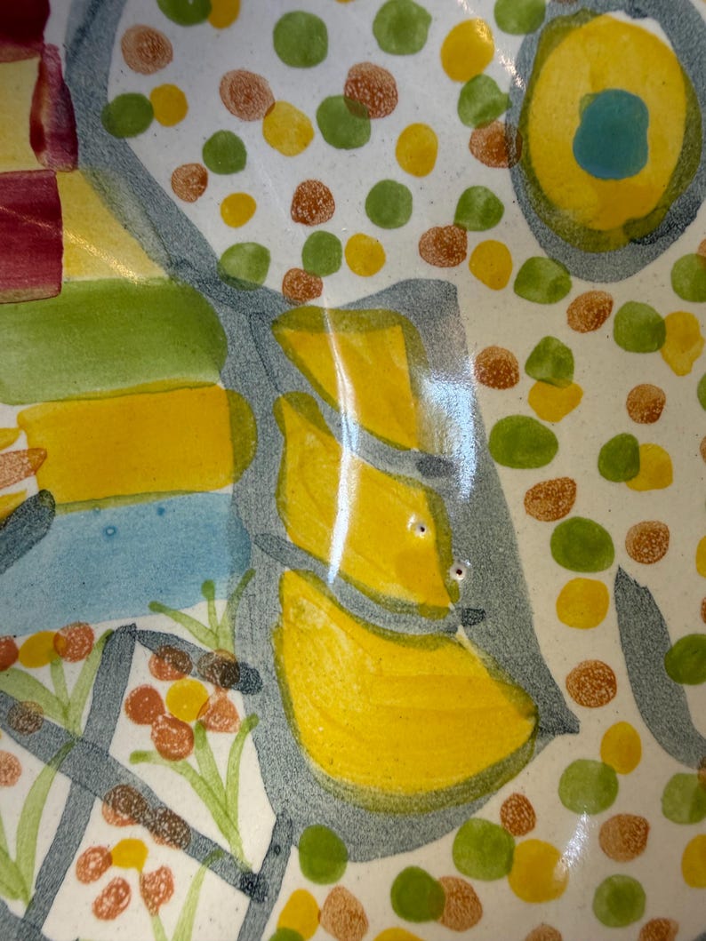 Puede incluir: Un cuenco de cer&aacute;mica con un dise&ntilde;o abstracto pintado a mano sobre una base blanca. La superficie est&aacute; decorada con puntos circulares amarillos, verdes y marrones, junto con formas geom&eacute;tricas azules y amarillas y acentos lineales gris oscuro.