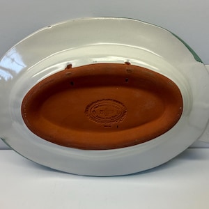 Puede incluir: La parte inferior de una bandeja de cer&aacute;mica con forma de pez, con un acabado esmaltado blanco y una base central ovalada de terracota sin esmaltar. La secci&oacute;n de terracota tiene una marca de fabricante estampada y dos orificios para colgar.