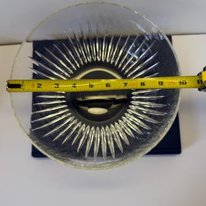 May include: Clear glass bowl with a starburst design in the center. The bowl is approximately 10 inches in diameter. The bowl is sitting on a dark blue surface.