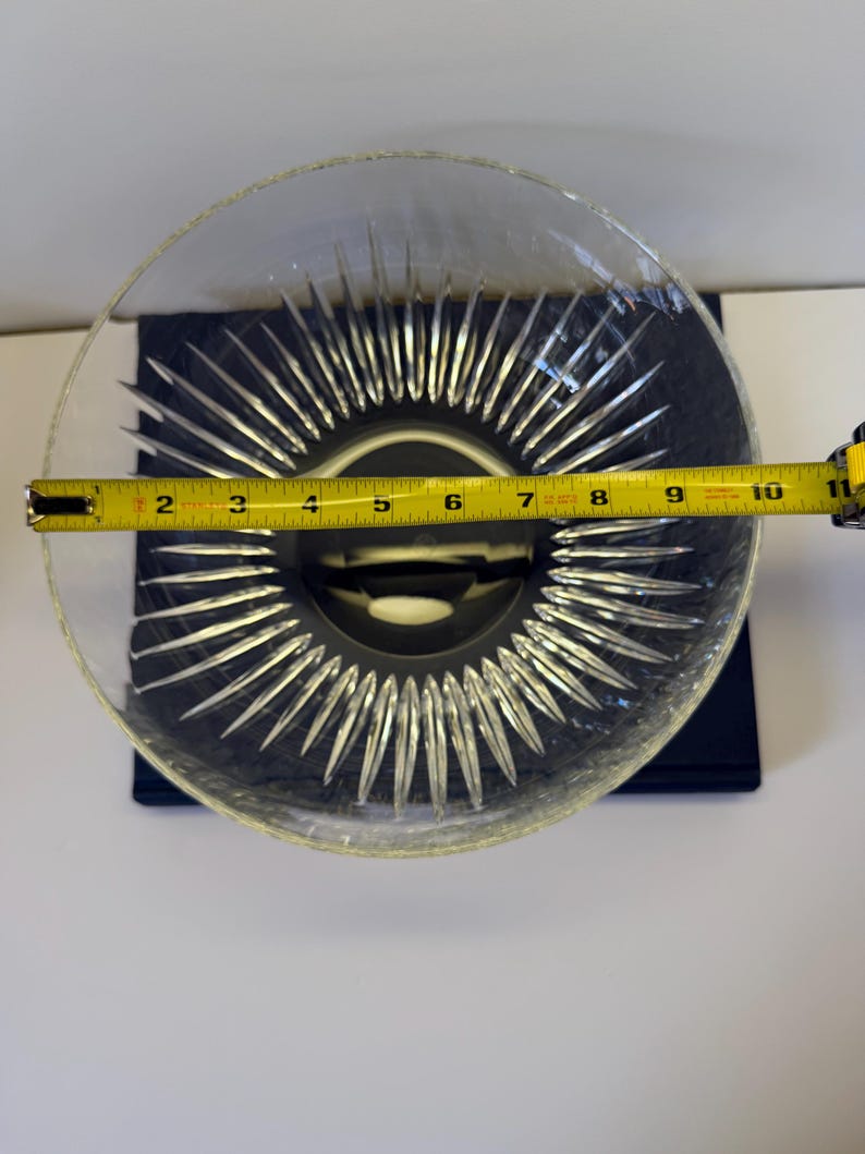May include: Clear glass bowl with a starburst design in the center. The bowl is approximately 10 inches in diameter. The bowl is sitting on a dark blue surface.