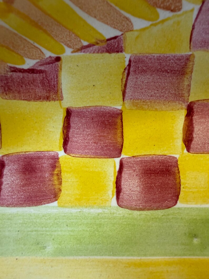 Puede incluir: Una superficie de cer&aacute;mica con un patr&oacute;n de tablero de ajedrez pintado a mano de cuadrados amarillos y granates oscuros alternos. Debajo de la secci&oacute;n a cuadros, hay bandas horizontales de pintura verde claro y amarilla con texturas visibles.