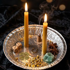 May include: Two lit yellow candles on a silver tray with dice, a horseshoe, four-leaf clover, star anise, and a green crystal. Smoke rises from the candles, suggesting a ritual or spiritual theme.